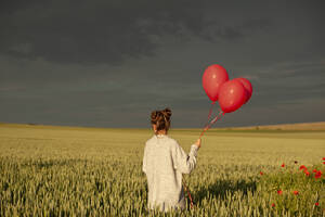 Mädchen hält rote Luftballons auf grünem Feld bei Sonnenuntergang - ALKF00145