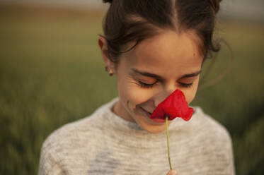 Smiling girl smelling poppy flower at sunset - ALKF00160