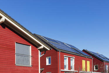 Deutschland, Nordrhein-Westfalen, Köln, Reihe von rot gestrichenen Holzhäusern mit Solardachplatten - GWF07733