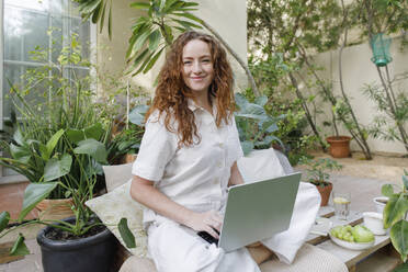 Smiling freelancer with cross-legged using laptop at backyard - TYF00766