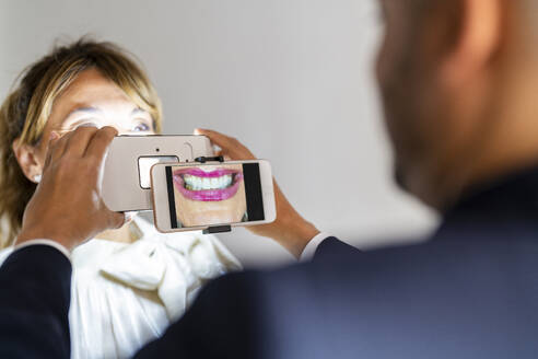 Geschäftsmann fotografiert das Lächeln eines Kollegen mit einem Smartphone und einer Vergrößerungsanlage - DLTSF03543
