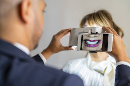 Geschäftsmann fotografiert das Lächeln eines Kollegen mit dem Mobiltelefon unter Verwendung eines Vergrößerungsgeräts - DLTSF03544