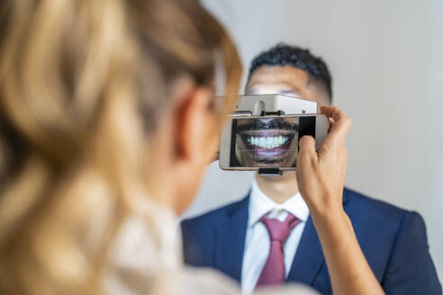 Geschäftsfrau fotografiert das Lächeln eines Kollegen mit dem Mobiltelefon unter Verwendung eines Vergrößerungsgeräts - DLTSF03545