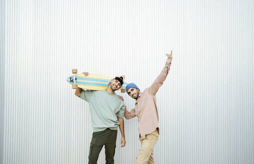 Two men standing with longboard in front of white wall - RCPF01687