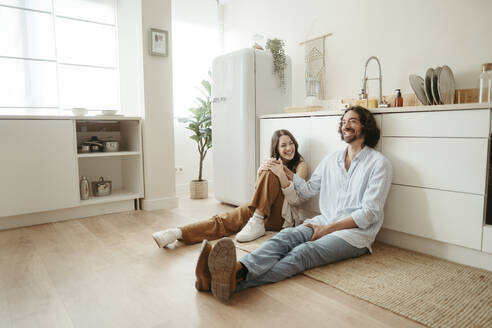 Glückliches Paar sitzt auf dem Boden in der Küche zu Hause - RCPF01715