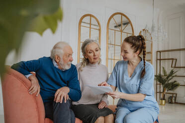 Glückliche Krankenschwester, die älteren Menschen zu Hause medizinische Berichte erklärt - MDOF00699