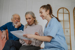 Glückliche Krankenschwester mit medizinischen Berichten von älterem Mann und Frau zu Hause - MDOF00702