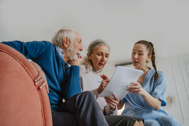 Pflegekraft hilft älteren Patienten bei der Unterzeichnung eines Dokuments zu Hause - MDOF00706