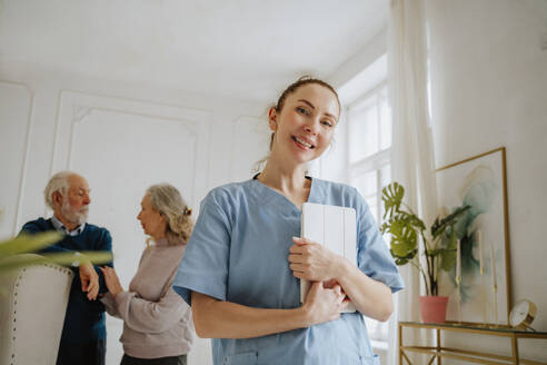 Smiling nurse holding tablet PC with senior man and woman at home - MDOF00722