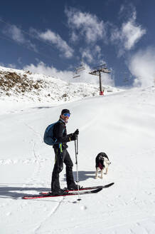 Lächelnder Mann mit Skistöcken und Hund im Schnee stehend - PGF01465