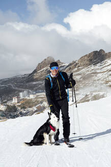 Mann mit Skistöcken und Hund im Schnee stehend - PGF01466