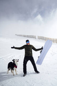 Glücklicher Mann mit Snowboard neben einem Hund im Urlaub - PGF01478