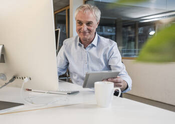 Smiling senior businessman with tablet PC using computer at office - UUF28260