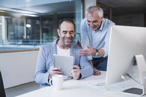 Glückliche Geschäftskollegen teilen sich einen Tablet-PC im Büro - UUF28269