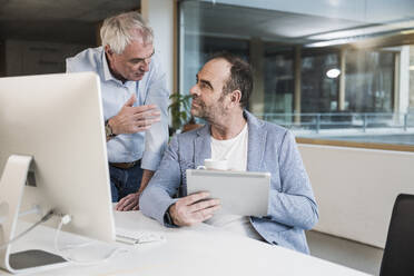 Geschäftsmann, der einem Kollegen erklärt, wie er einen Tablet-PC im Büro hält - UUF28270