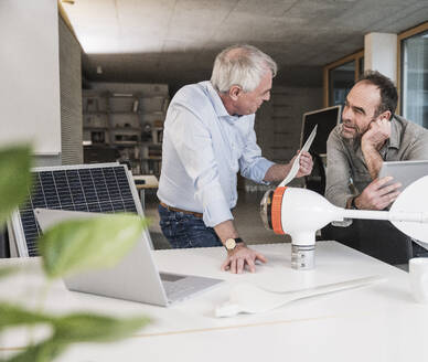 Engineer discussing with colleague over wind turbine rotor at office - UUF28281
