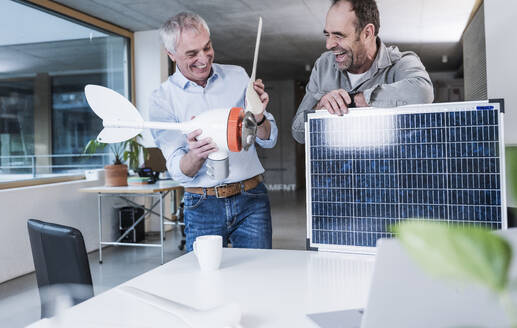 Glücklicher leitender Ingenieur bei der Arbeit mit einem Kollegen mit Solarpanel im Büro - UUF28286