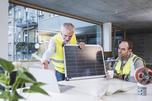 Engineer with solar panel explaining colleague over tablet PC at office - UUF28293