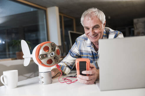 Smiling engineer examining current of wind turbine rotor at office - UUF28301