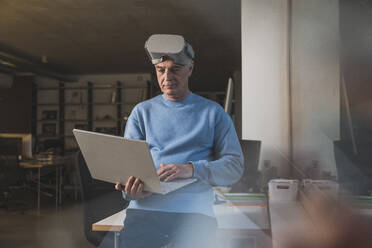 Geschäftsmann mit Virtual-Reality-Headset und Laptop im Büro - UUF28303