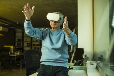 Senior businessman wearing virtual reality headset and gesturing at office - UUF28308