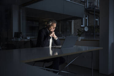 Geschäftsmann beobachtet Laptop am Schreibtisch im Büro sitzend - UUF28335