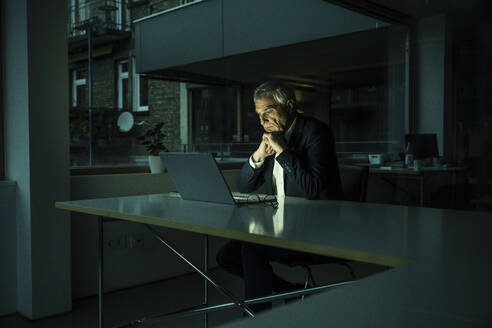 Businessman watching laptop at late night at workplace - UUF28336