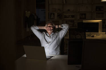 Senior businessman with hands behind head relaxing at office - UUF28339