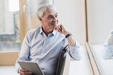 Thoughtful businessman with hand on chin looking out of window at workplace - UUF28354