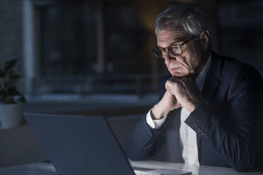 Seriöser älterer Geschäftsmann beobachtet Laptop im Büro bei der Arbeit - UUF28355