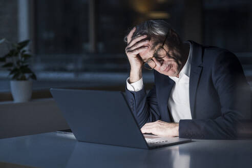 Frustrated businessman with head in hand watching laptop at office - UUF28356