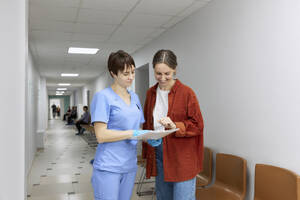 Doctor and patient reviewing test results standing in corridor at hospital - SANF00061