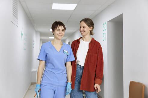 Ein lächelnder Patient steht mit einem Arzt auf dem Korridor eines Krankenhauses - SANF00062