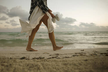 Woman walking barefoot on sand near shore at beach - IEF00282