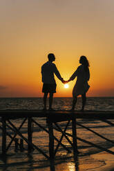 Silhouette of couple holding hands and standing on pier at sunrise - IEF00283