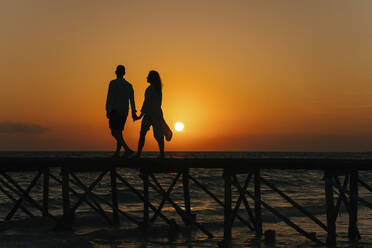 Silhouette of couple walking on pier at sunrise - IEF00284