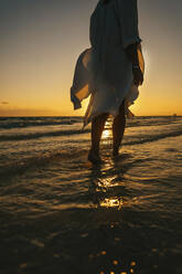 Frau spaziert im Meer am Strand bei Sonnenaufgang - IEF00289