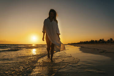 Unbekümmerte Frau, die bei Sonnenaufgang am Strand spazieren geht - IEF00290