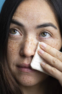 Woman with freckles cleaning face with makeup wipe - MRAF00921
