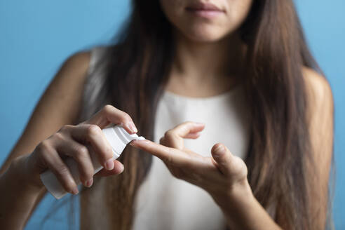 Woman applying cream on finger against blue background - MRAF00922