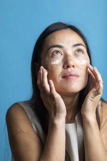 Woman applying cream on face against colored background - MRAF00923