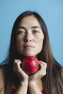 Woman holding pomegranate fruit against blue background - MRAF00931