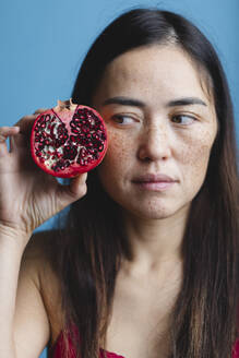 Woman holding pomegranate against blue background - MRAF00934