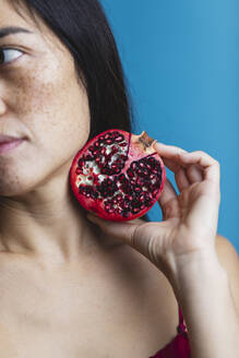 Woman holding pomegranate against blue background - MRAF00935