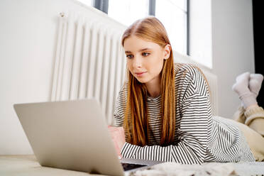 Teenager-Mädchen mit rotem Kopf, das einen zu Hause liegenden Laptop benutzt - MDOF00724