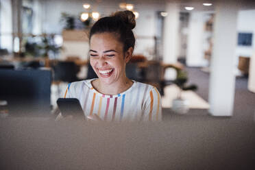 Cheerful businesswoman using mobile phone in office - JOSEF17422