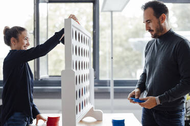 Happy businesswoman with colleague playing connect four dots game in office - JOSEF17447