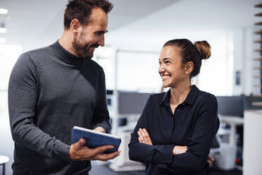 Happy businessman discussing over tablet PC with colleague in office - JOSEF17463