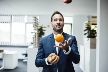 Geschäftsmann jongliert mit Orangenfrüchten im Büro - JOSEF17513