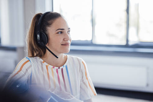 Smiling businesswoman wearing headset at office - JOSEF17526